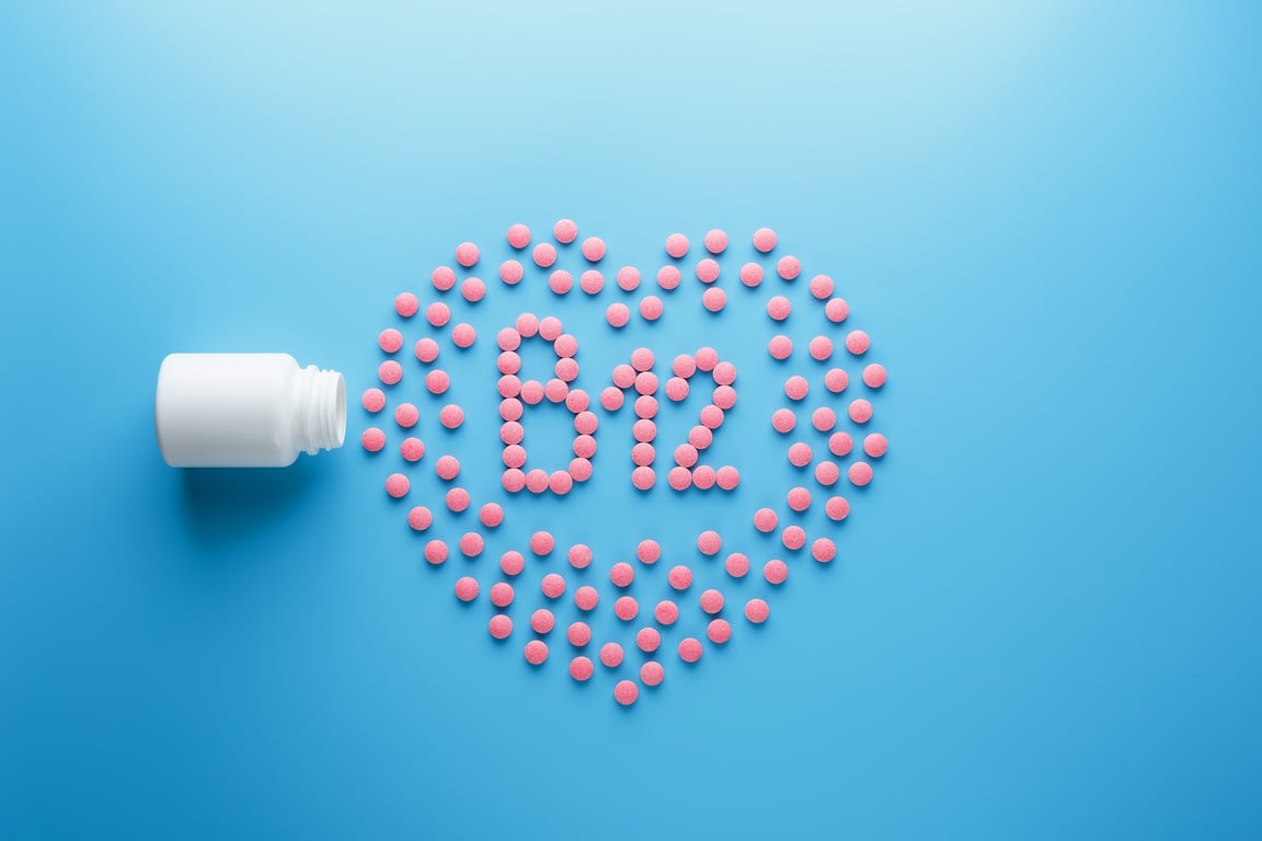 Pink tablets in the form of B12 in the heart on a blue background, spilled from a white can.